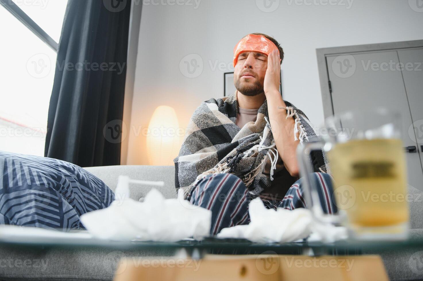 ein krank Mann sitzt beim Zuhause auf ein grau Sofa mit ein Decke. Erkrankung, Schutz, Coronavirus, Erkrankung, Grippe foto