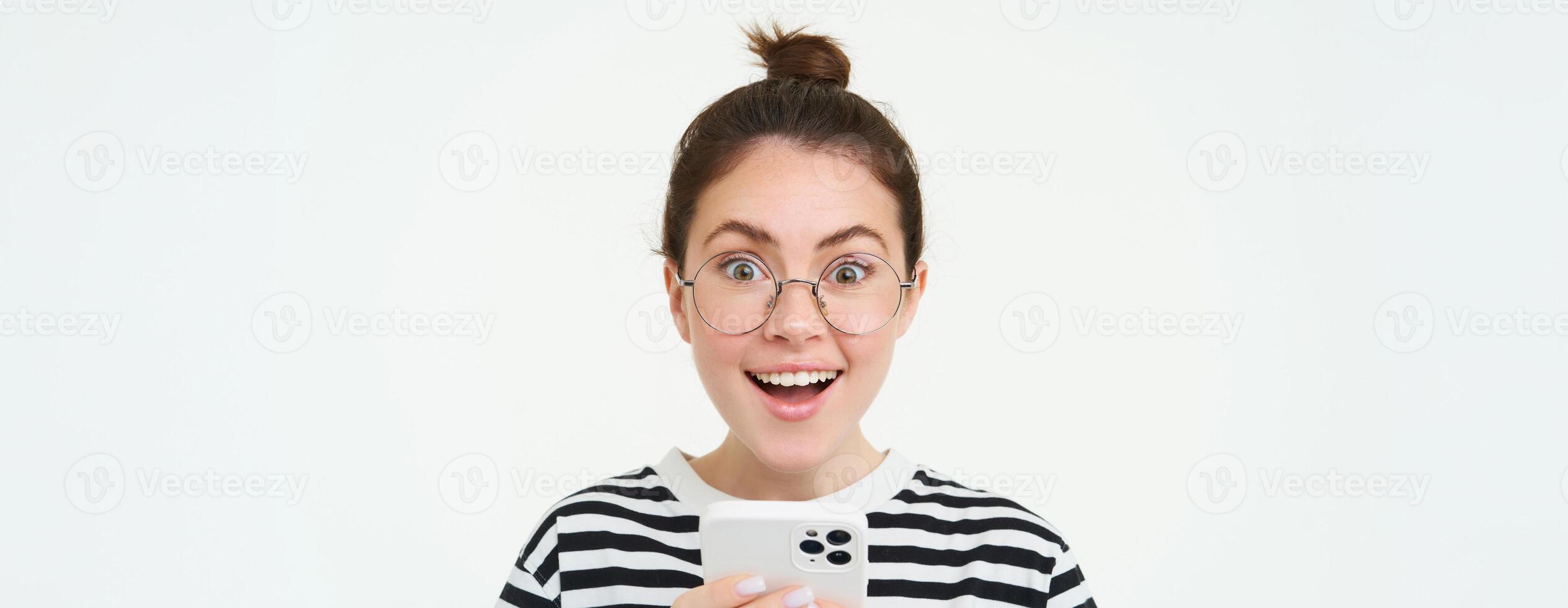 Bild von jung Frau im Gläser, mit ihr Handy, Mobiltelefon Telefon, Stehen mit Smartphone und lächelnd, Stehen Über Weiß Hintergrund foto