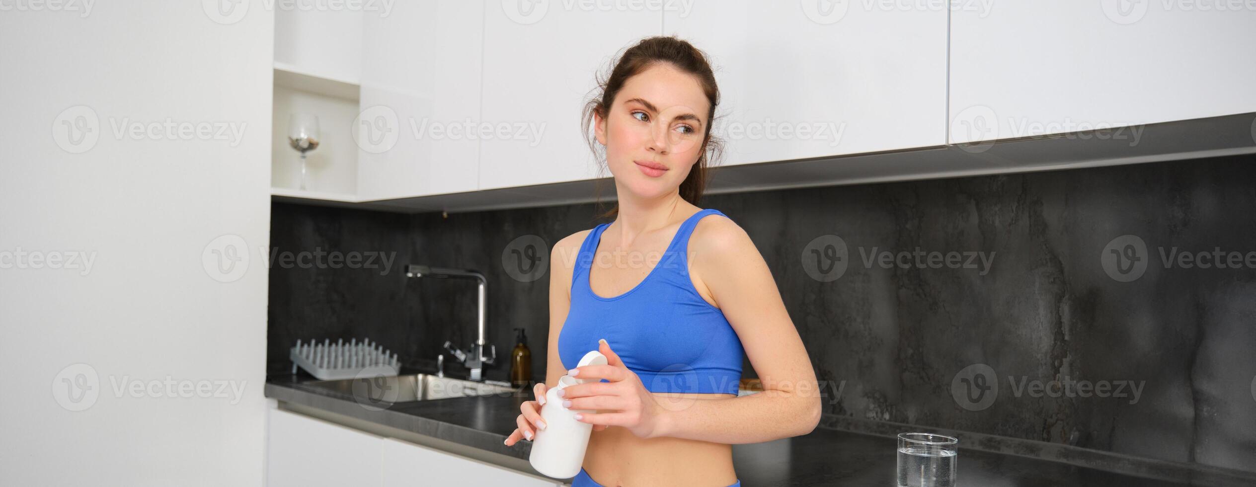 Porträt von gesund, schön Frau, halten Flasche von Vitamine, nehmen Diät Ergänzungen, Knospen zum glänzend Haut und stark Muskeln, Stehen im Fitness Kleidung foto