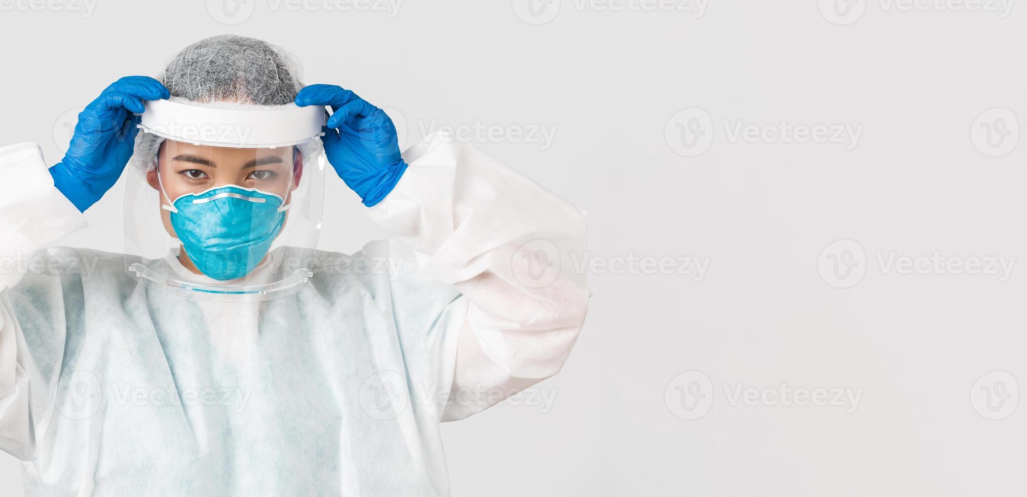 COVID-19, Coronavirus Krankheit, Gesundheitswesen Arbeitskräfte Konzept. zuversichtlich ernst aussehend asiatisch weiblich Arzt, stellen auf Gesicht Schild und persönlich schützend Ausrüstung Vor eintreten ansteckend Zone foto
