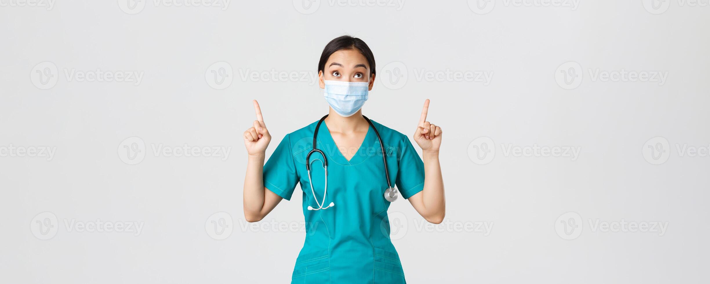COVID-19, Coronavirus Krankheit, Gesundheitswesen Arbeitskräfte Konzept. fasziniert und aufgeregt asiatisch Frau Arzt, Krankenschwester im medizinisch Maske und Handschuhe, suchen und zeigen Finger hoch, Weiß Hintergrund foto