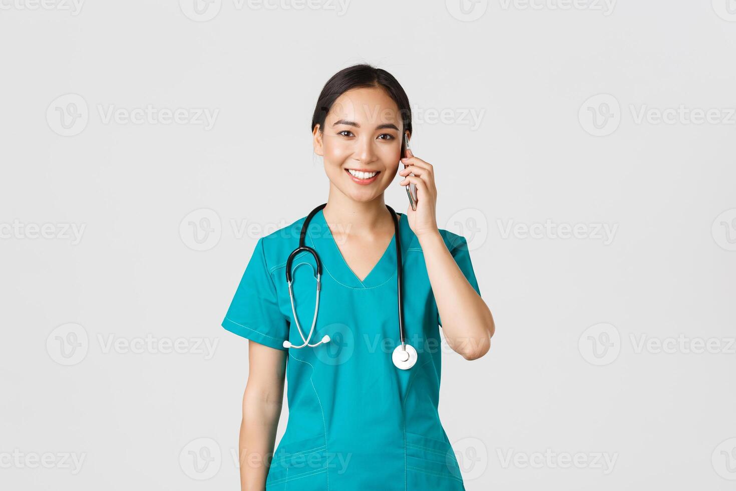 COVID-19, Gesundheitswesen Arbeitskräfte und verhindern Virus Konzept. lächelnd glücklich asiatisch weiblich Arzt, jung Praktikant im Peelings reden auf Telefon, suchen beim Kamera hoffnungsvoll, Weiß Hintergrund foto
