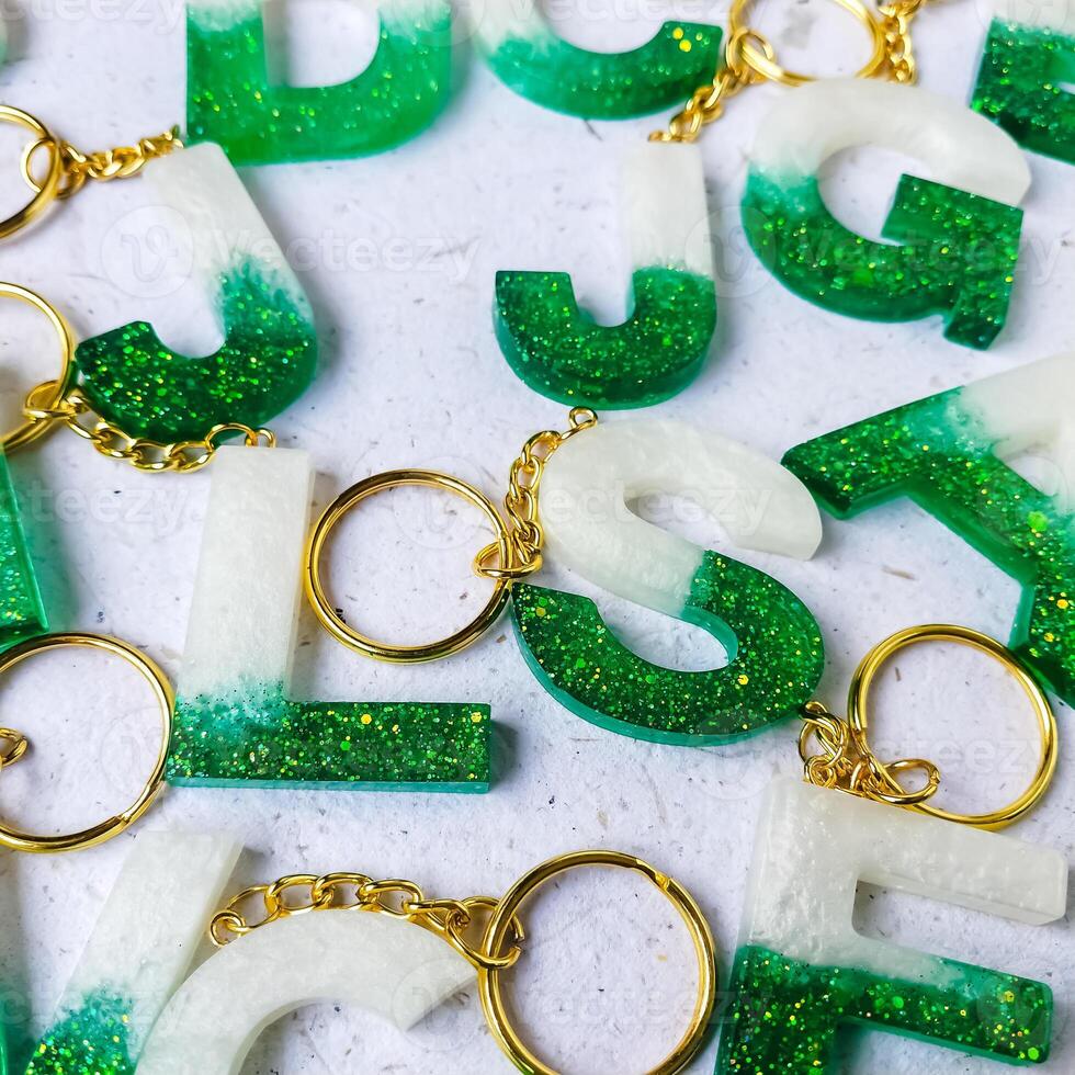 Grün funkeln Briefe mit Perlen. golden Schlüsselbund auf Weiß Papier Hintergrund mit getrocknet Blumen. oben Sicht. Harz Handwerk. foto