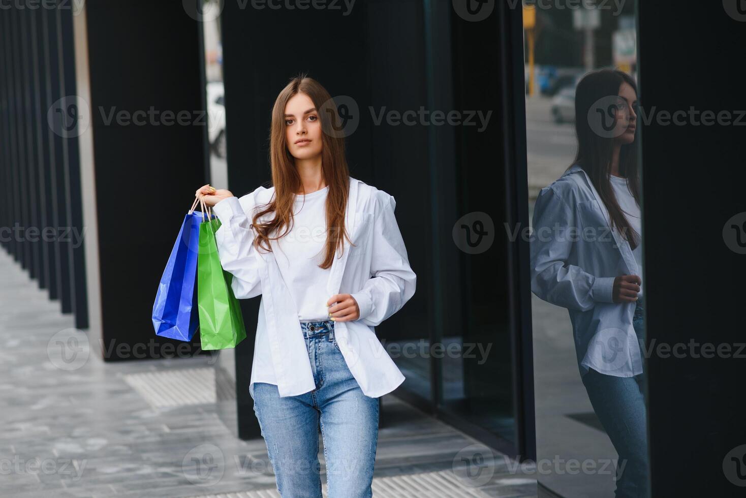 modisch schön glücklich Frau Stehen mit Einkaufen Taschen in der Nähe von ein Einkaufen Center auf schwarz Freitag. foto