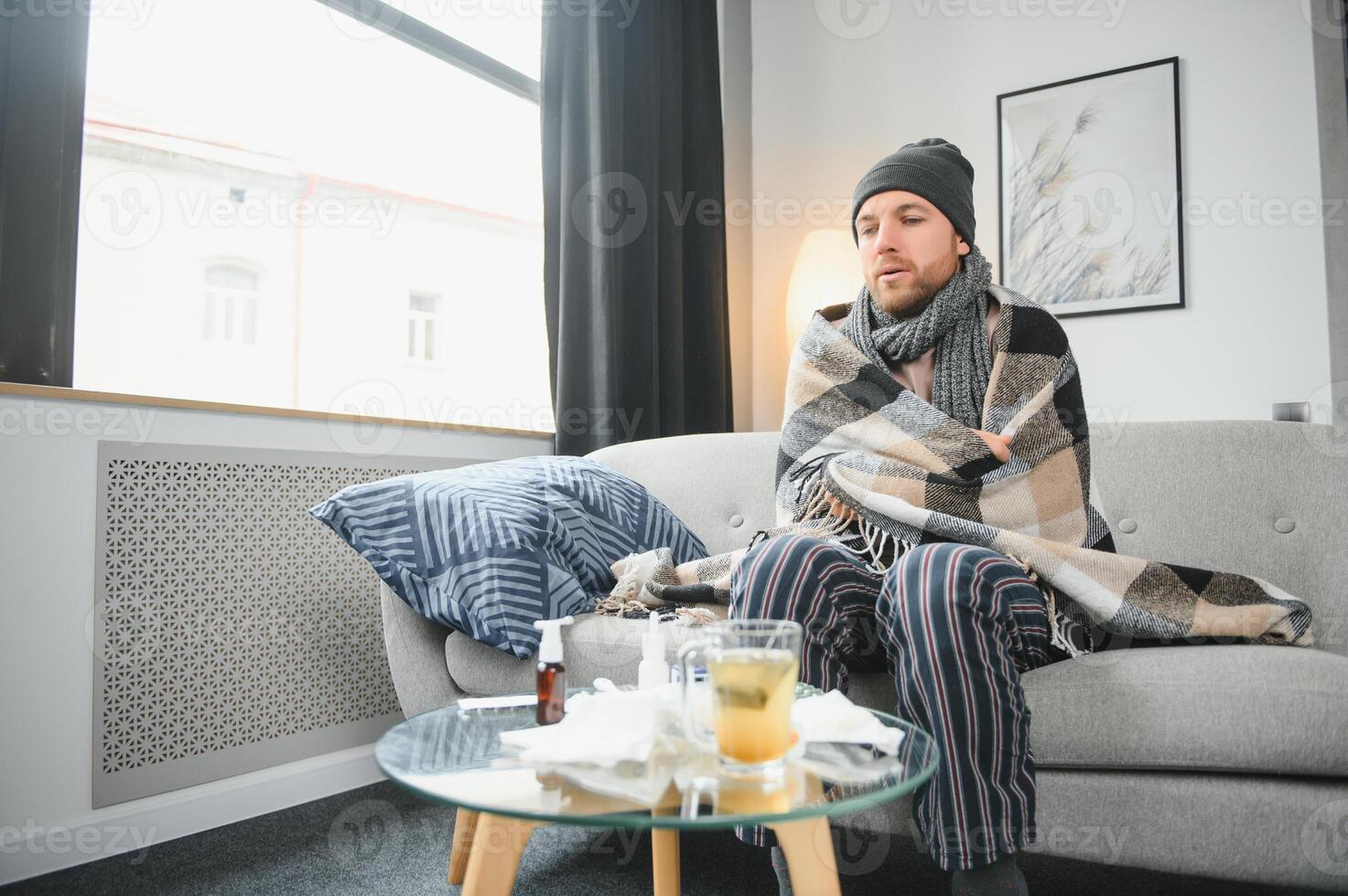 es ist kalt beim Zuhause im Winter. Mann Einfrieren im seine Haus im Winter weil von gebrochen Thermostat. jung Kerl eingewickelt im Wolle Plaid Zittern während Sitzung auf Sofa im Leben Zimmer Innere foto