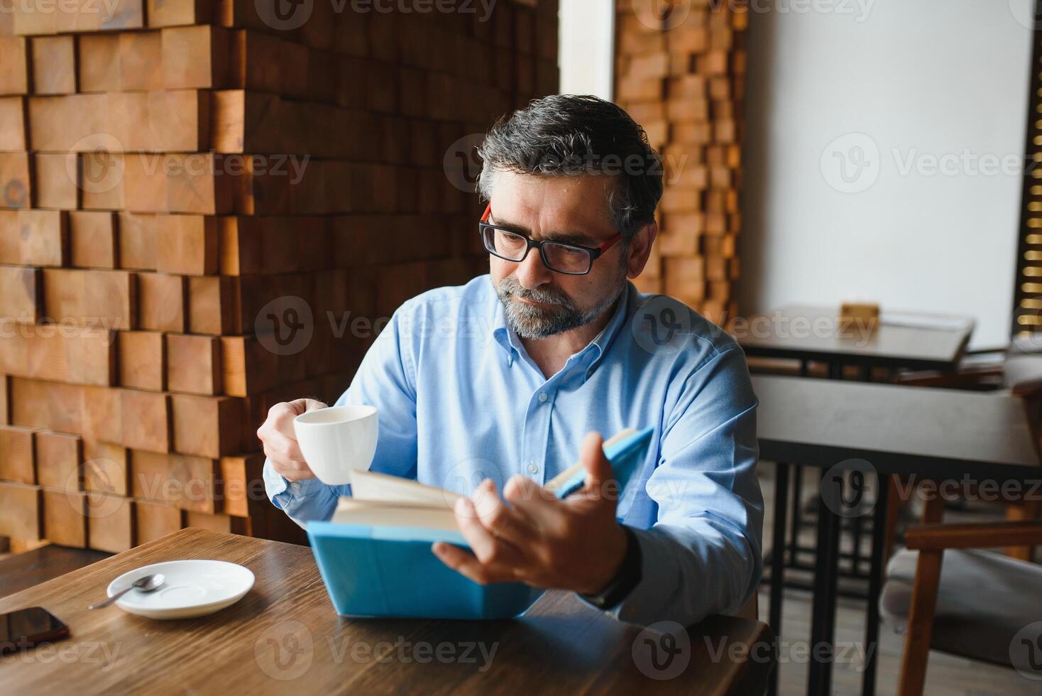 reifen gut aussehend Mann lesen ein Buch im ein Cafe foto