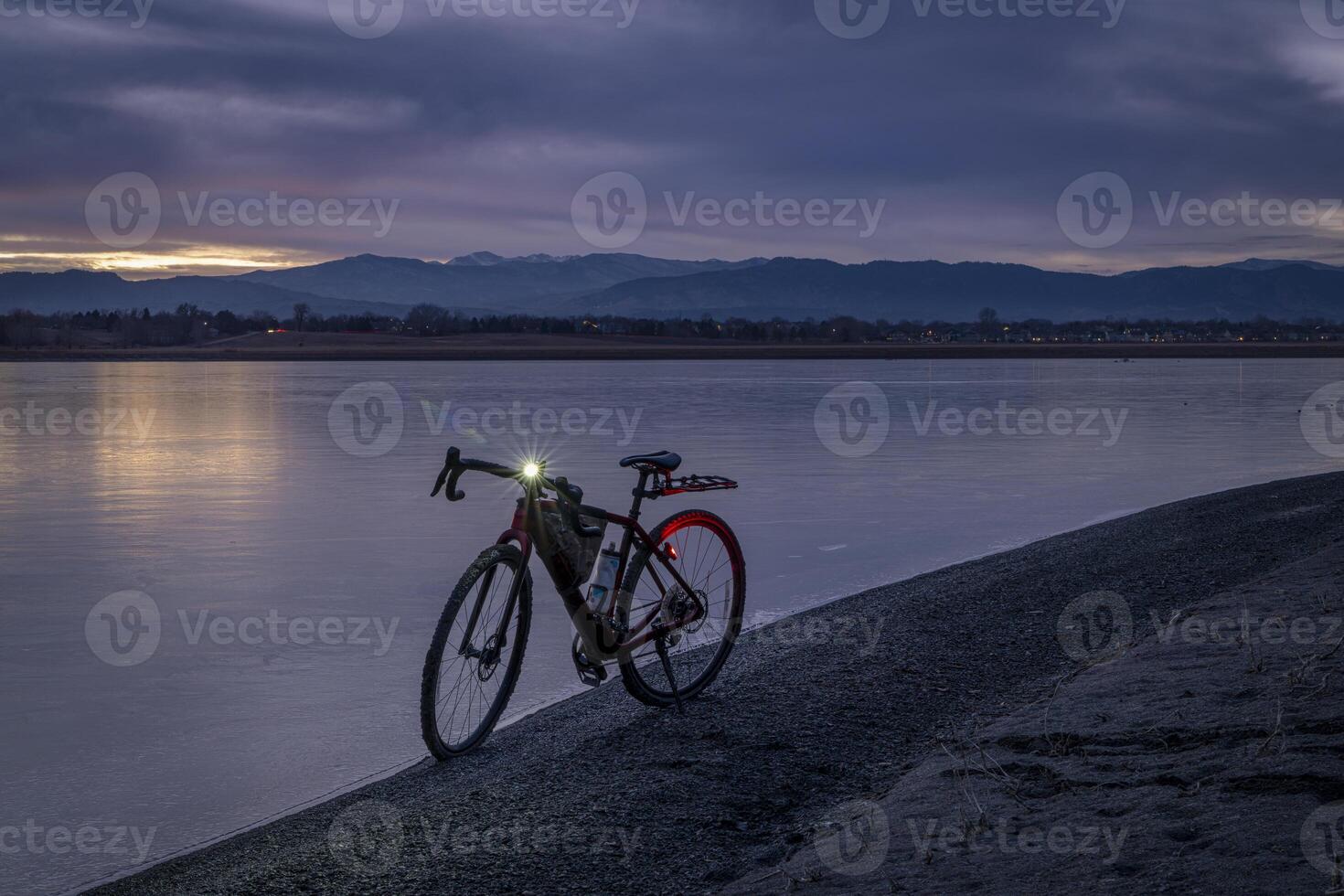 Kies Fahrrad auf ein Ufer von ein gefroren See mit entfernt Aussicht von felsig Berge, Winter Dämmerung im Nord Colorado foto