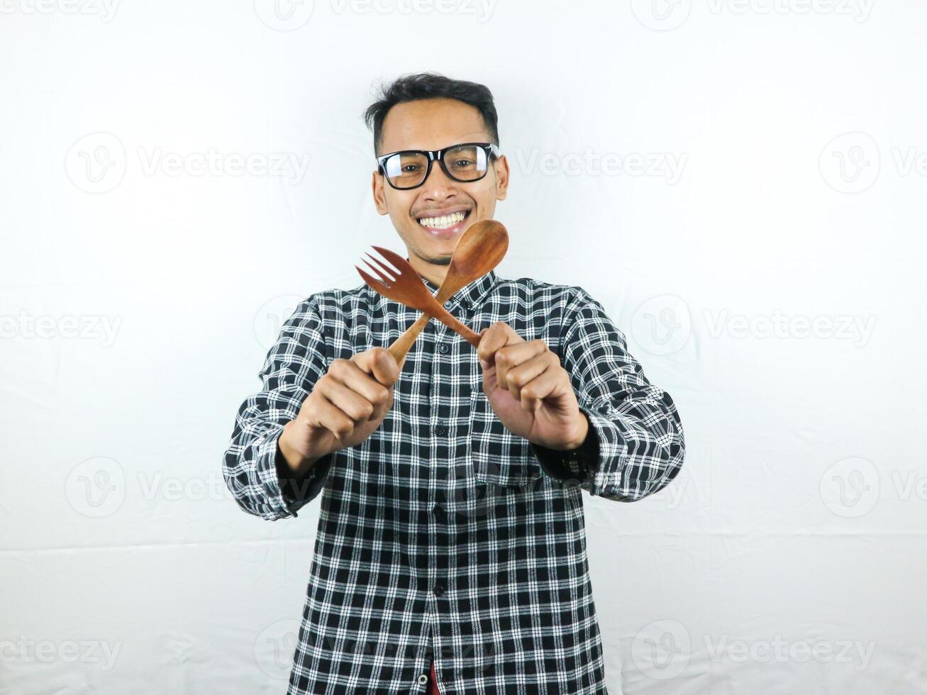 aufgeregt asiatisch Mann halten Löffel und Gabel im seine Hände foto
