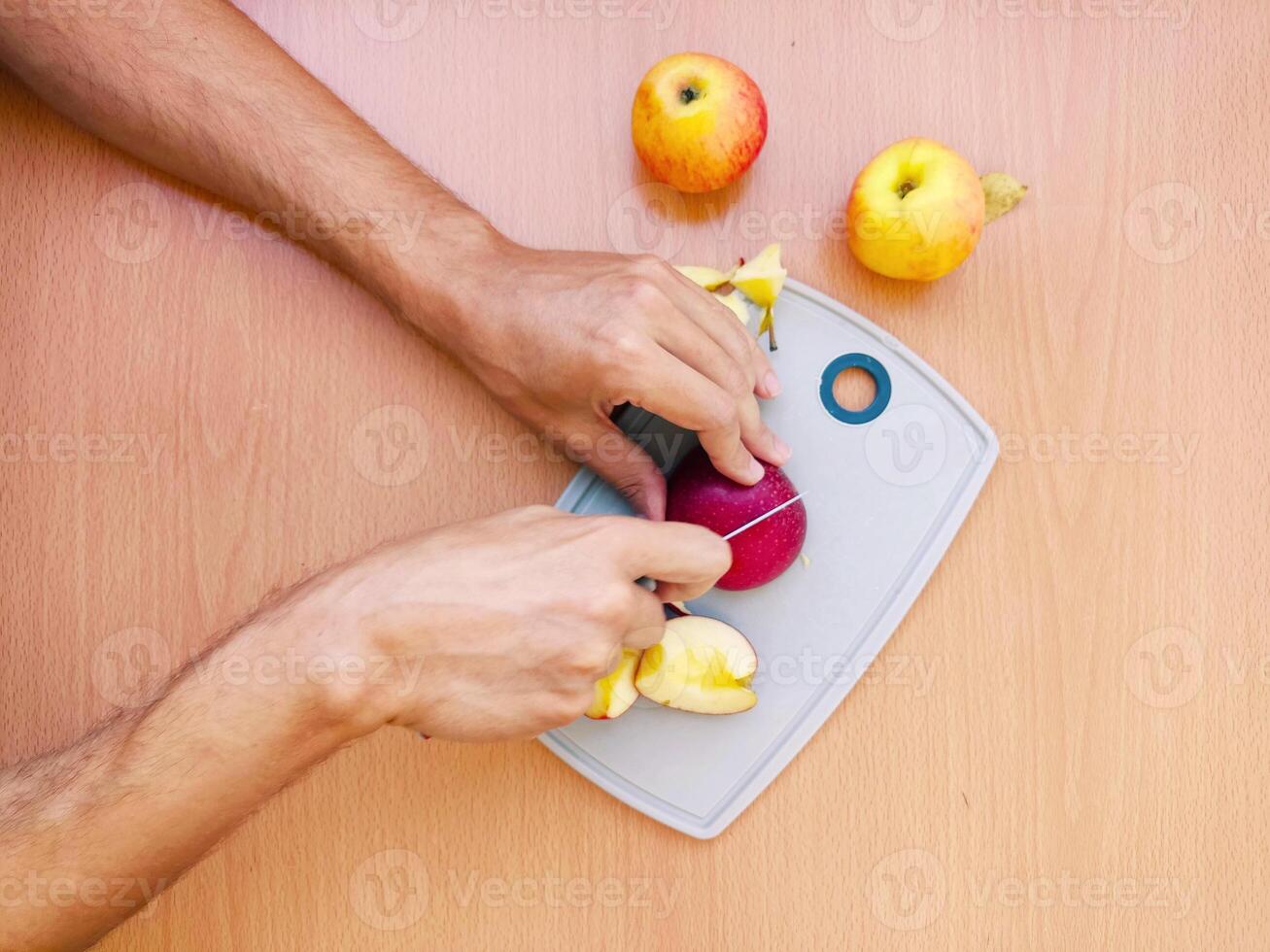 schließen oben männlich Hände Schnitt ein Apfel in Scheiben. oben Aussicht von vorbereiten Früchte Über Küche Tisch. foto