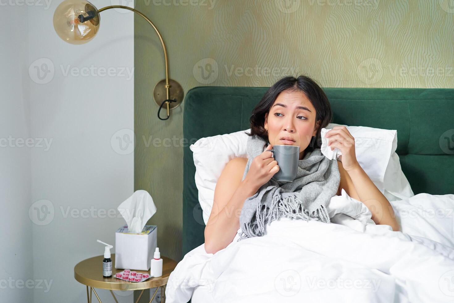 krank traurig asiatisch Mädchen Lügen im ihr Bett mit Grippe, Fang ein kalt, nehmen Tabletten und Trinken heiß Tee, Gefühl verärgert foto