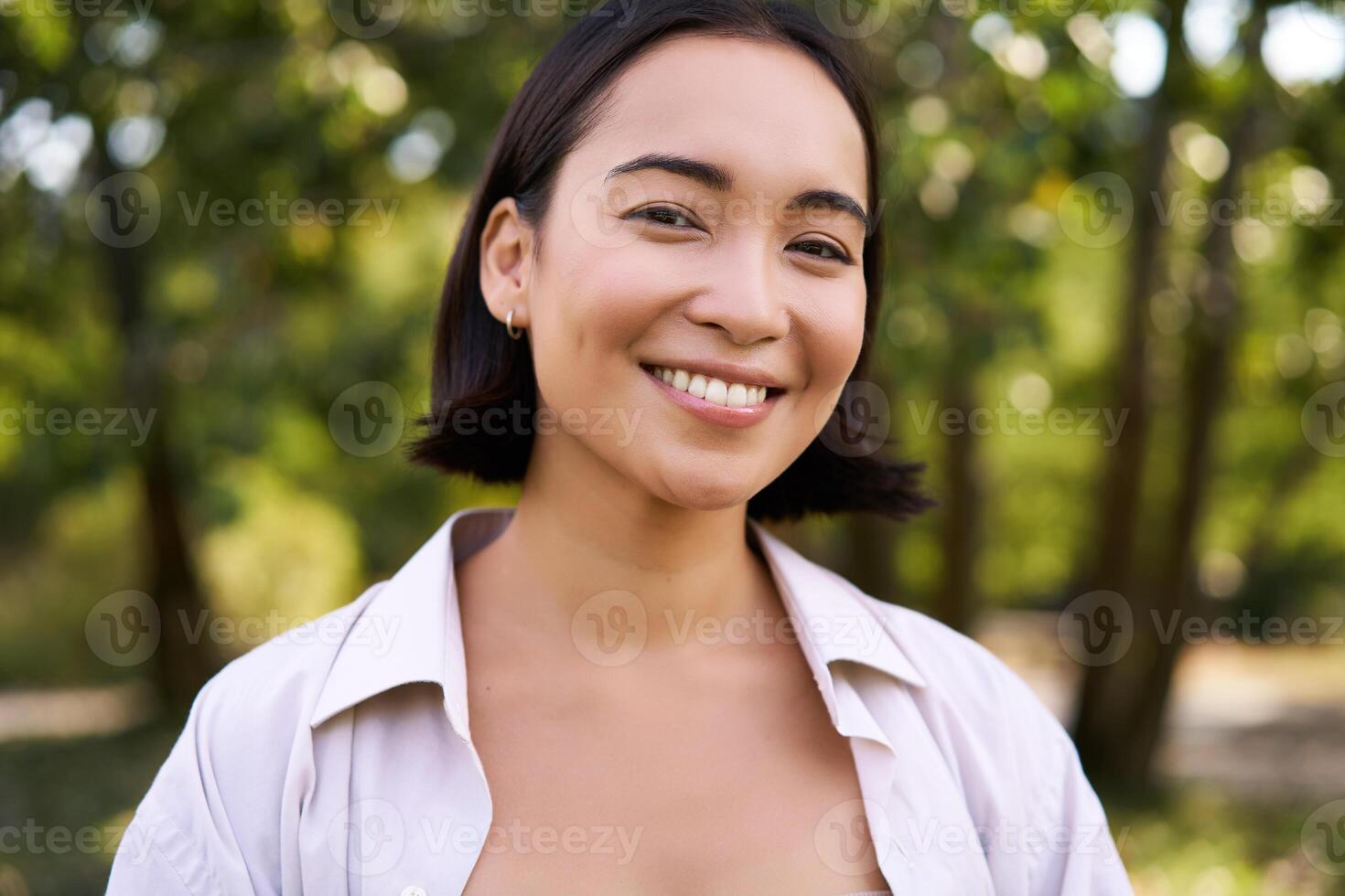 Menschen Konzept. lächelnd asiatisch Mädchen suchen beim Kamera mit Glücklich, froh Emotion, posieren im Grün Park auf ein warm Sommer- Tag foto