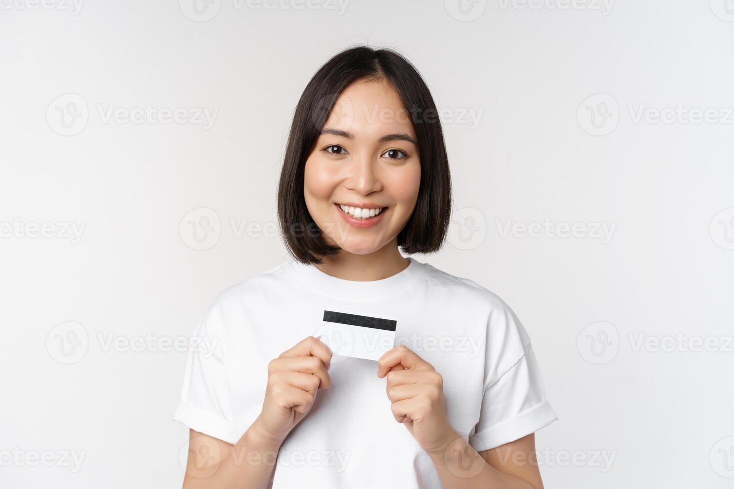 lächelnd Koreanisch Frau zeigen Anerkennung Karte mit glücklich Gesicht, Stehen im T-Shirt Über Weiß Hintergrund foto
