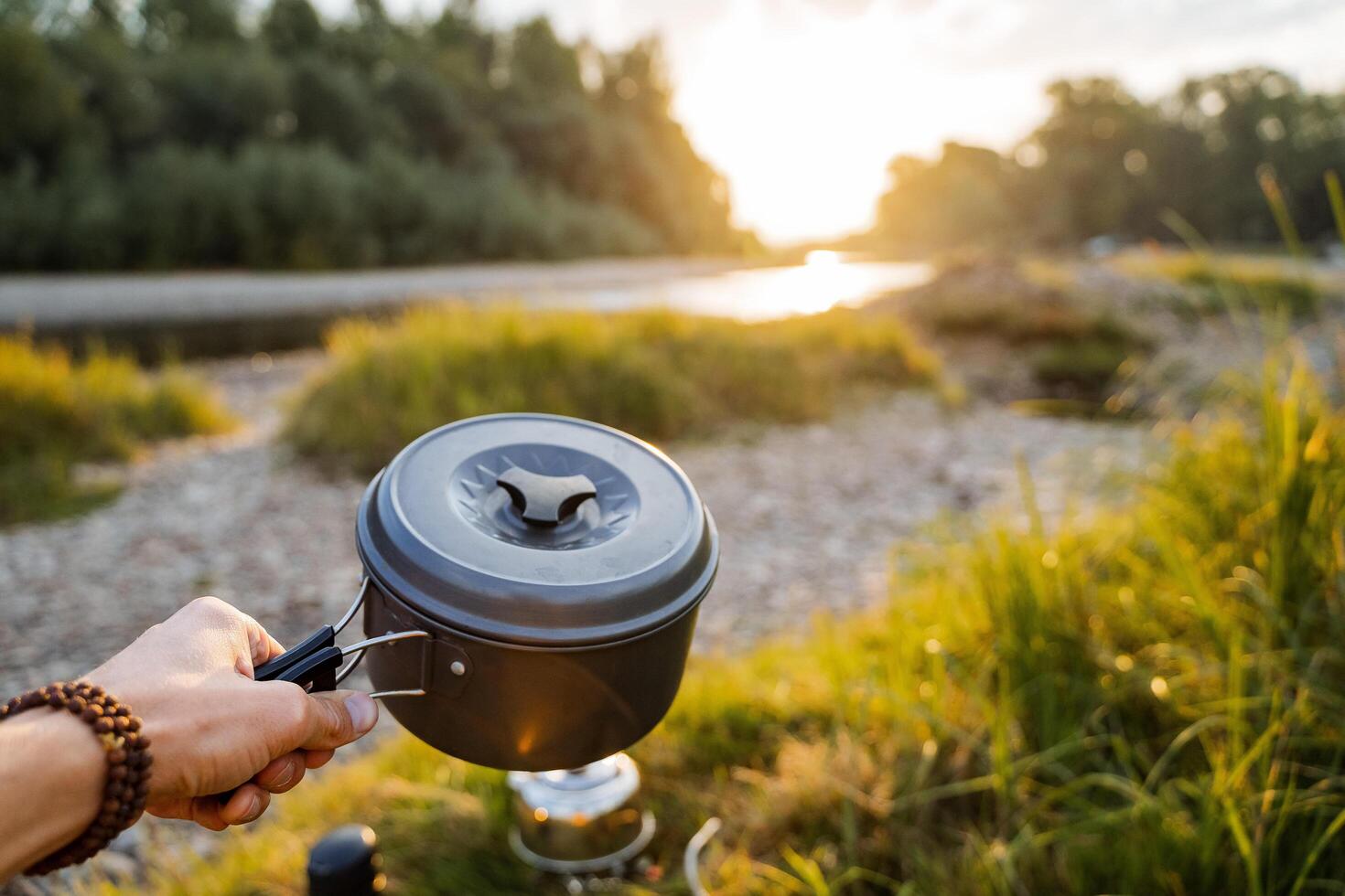 Mahlzeit im Natur. Topf -Topf im das Hände von ein Tourist, Fokus auf ihnen. voraus von das Fluss Landschaft und Grün Wald. in der Nähe Lügen das sich ausruhen von das Küche Camping Utensilien. Tourist Snack, draussen Aktivität foto