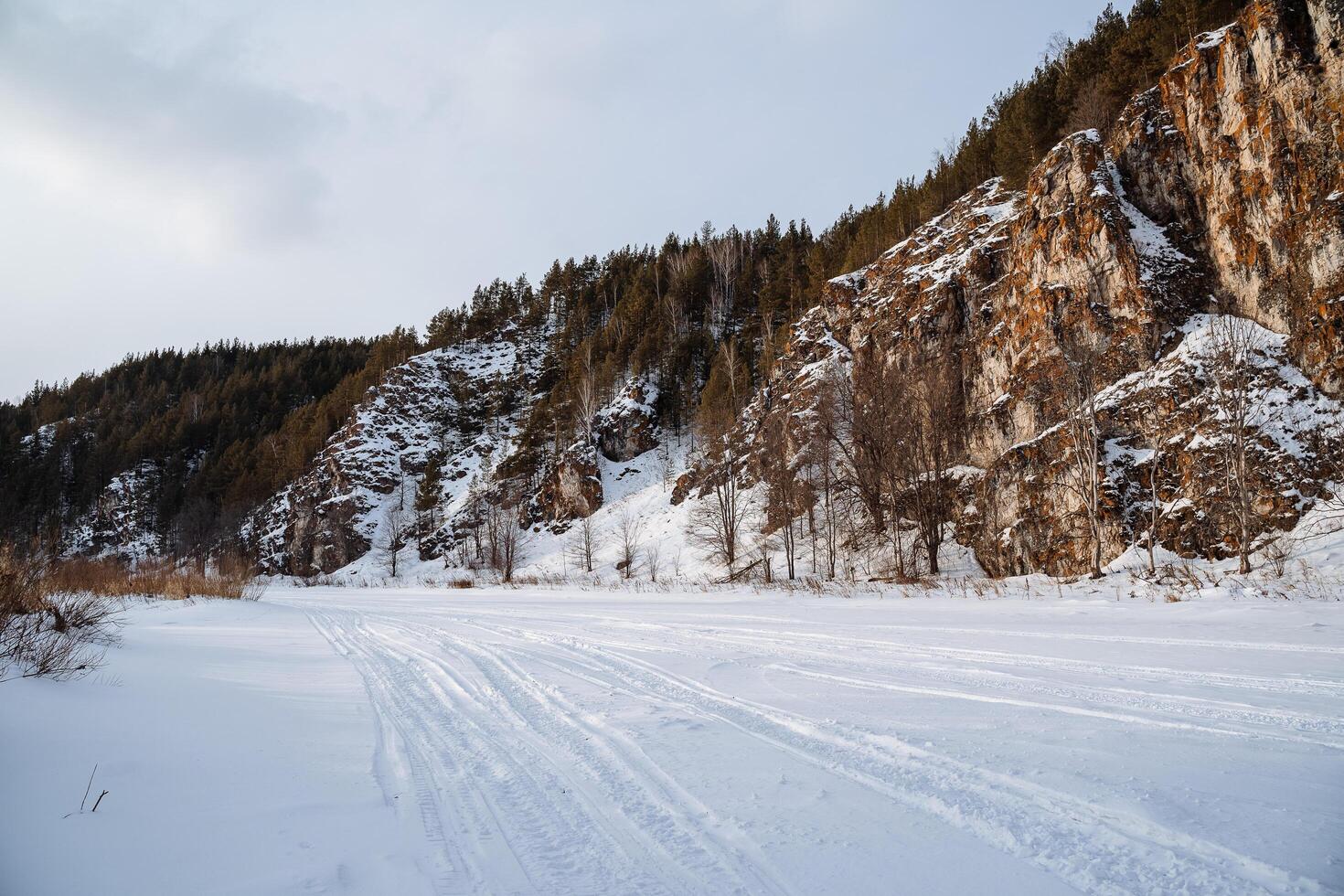 Winter im das Süd- Ural im das Tscheljabinsk Region. ein gefroren Fluss gegen das Hintergrund von Felsen. das eben Felsen ist bedeckt mit Orange Moos. Russisch Winter foto