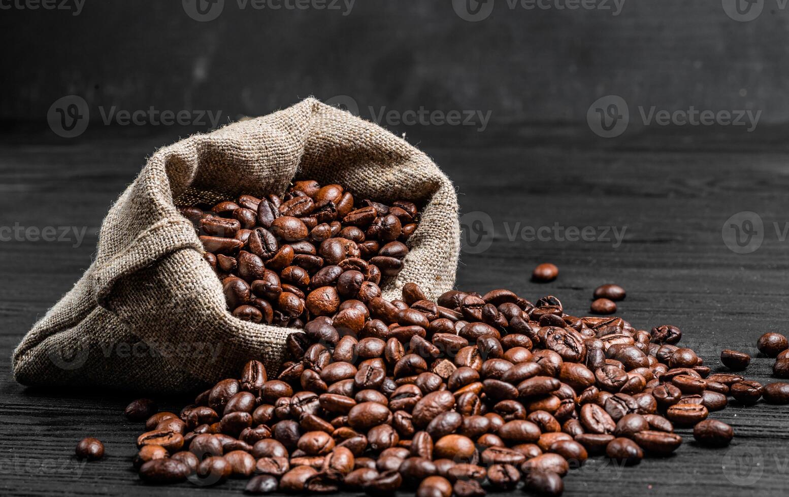 organisch Kaffee Saat Streuung von das Sack Über das dunkel hölzern Oberfläche. frisch Kaffee Bohnen in der Nähe von das Licht braun Sack isoliert. Nahansicht foto