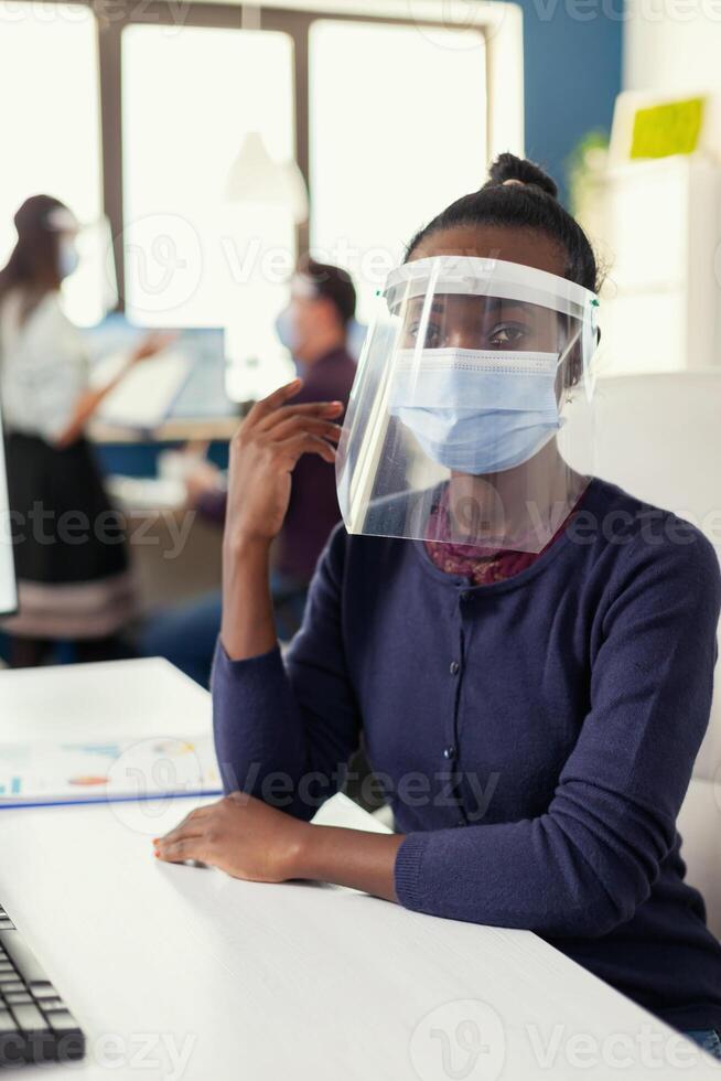 Unternehmer Sitzung beim ihr Arbeitsplatz tragen Gesicht Maske gegen Coronavirus. multiethnisch Geschäft Mannschaft Arbeiten im finanziell Unternehmen respektieren Sozial Entfernung während global Pandemie. foto