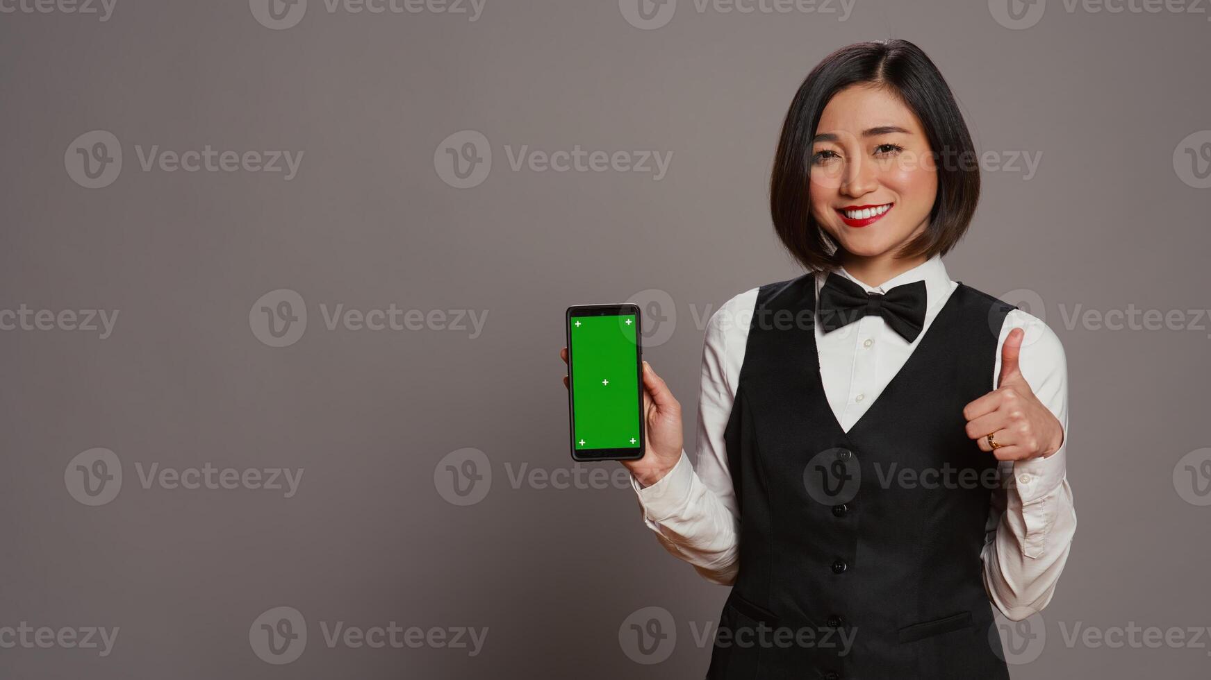 asiatisch Hotel Portier zeigen beim Telefon mit grüner Bildschirm Layout, halten Gerät Laufen isoliert Chromakey Vorlage. Rezeptionist zeigen Smartphone Anzeige mit Copyspace Attrappe, Lehrmodell, Simulation. Kamera b. foto