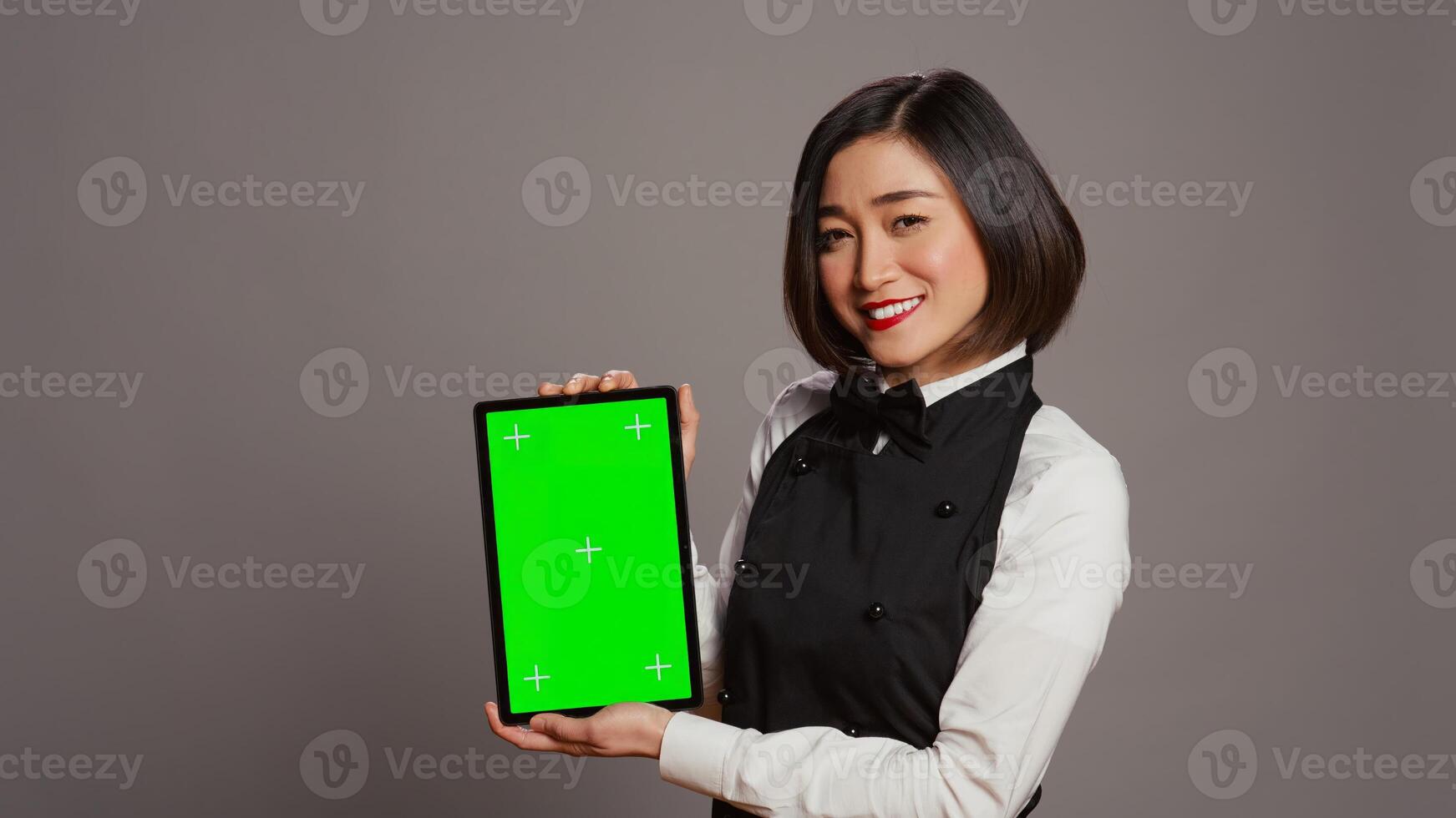 asiatisch Restaurant Hostess zeigen grüner Bildschirm Anzeige im Studio, präsentieren isoliert Attrappe, Lehrmodell, Simulation Layout auf Tablette. Kellnerin Arbeiten mit leer Copyspace Chromakey Vorlage auf Bildschirm. Kamera b. foto