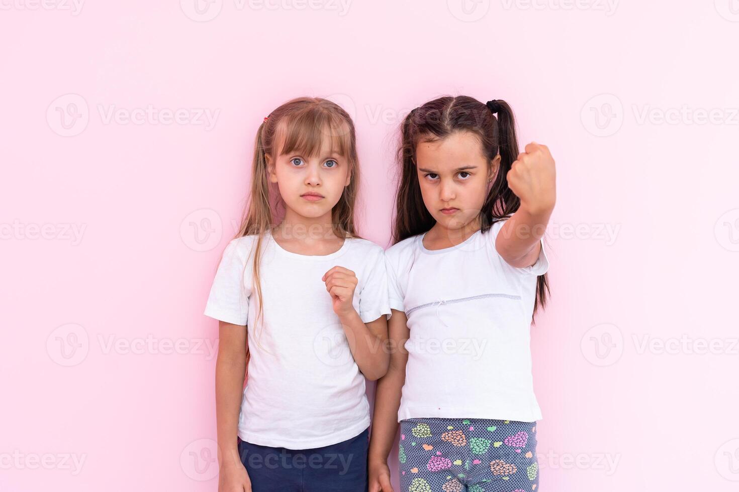 ziemlich zwei Kind Mädchen im Weiß T-Shirts mit lange Haar, aussehen beim Kamera und Nieder auf T-Shirt foto