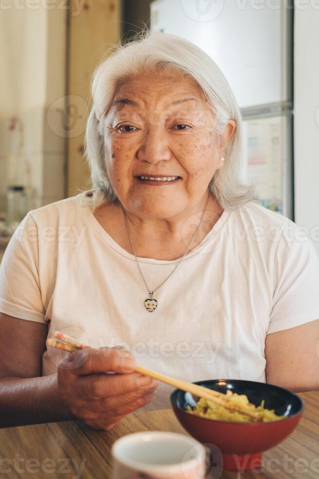 Senior Erwachsene japanisch Frau Essen Reis mit Essstäbchen sieht aus und lächelt beim Kamera foto