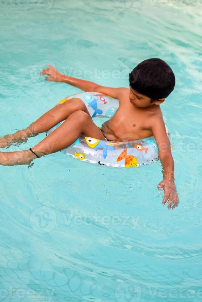 glücklich indisch Junge Schwimmen im ein Schwimmbad, Kind tragen Schwimmen Kostüm entlang mit Luft Tube während heiß Sommer- Urlaube, Kinder Junge im groß Schwimmen Schwimmbad. foto