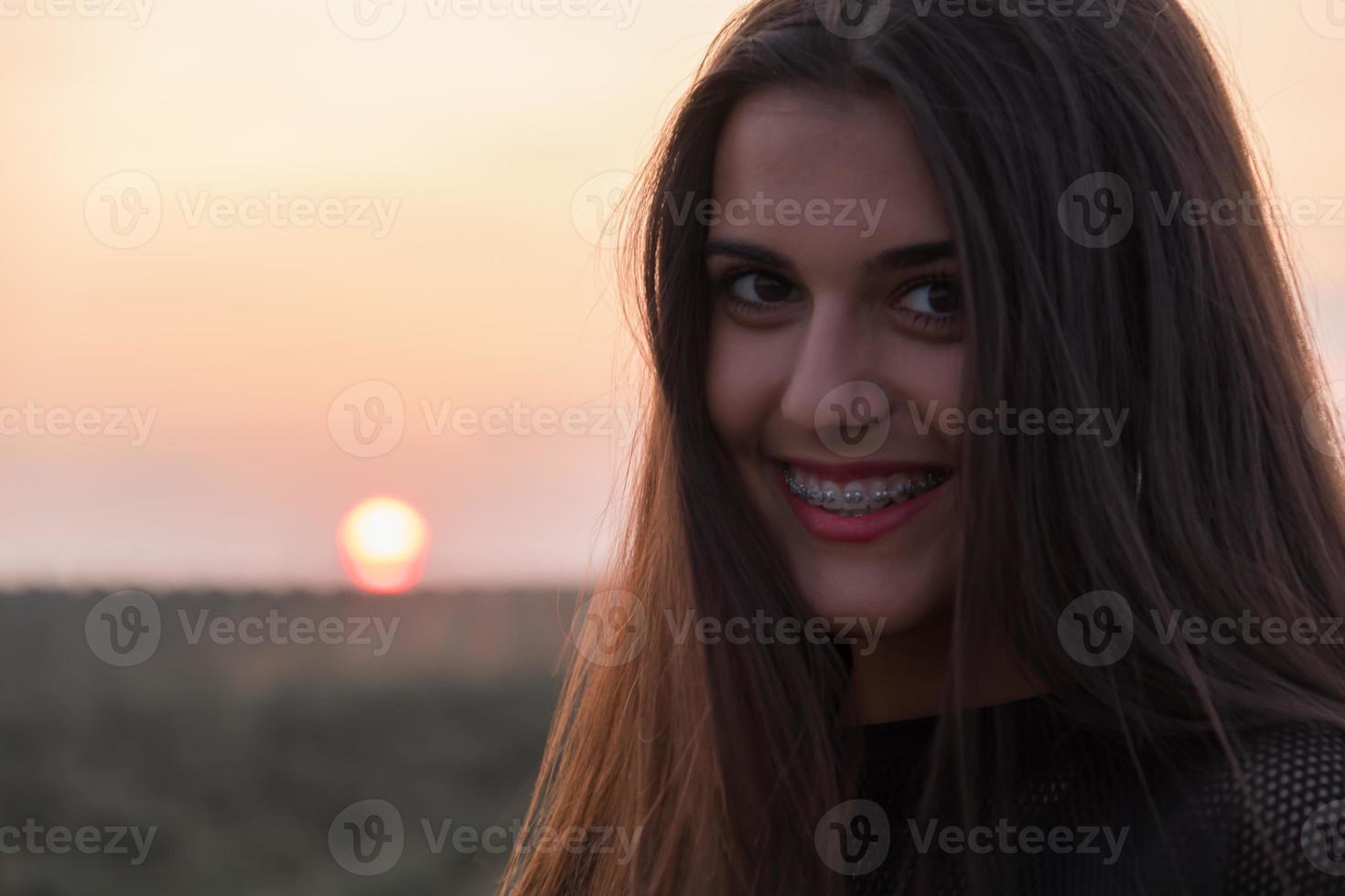 Schönes junges brünettes Mädchen, das bei Sonnenuntergang eine Straße mitten auf dem Feld aufwirft foto