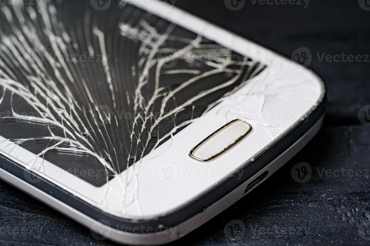 Nahansicht Teil von ein modern Smartphone mit geknackt Glas von berühren Bildschirm auf ein dunkel Hintergrund. teuer Weiß gebrochen Handy, Mobiltelefon Telefon. Makro Schuss. foto