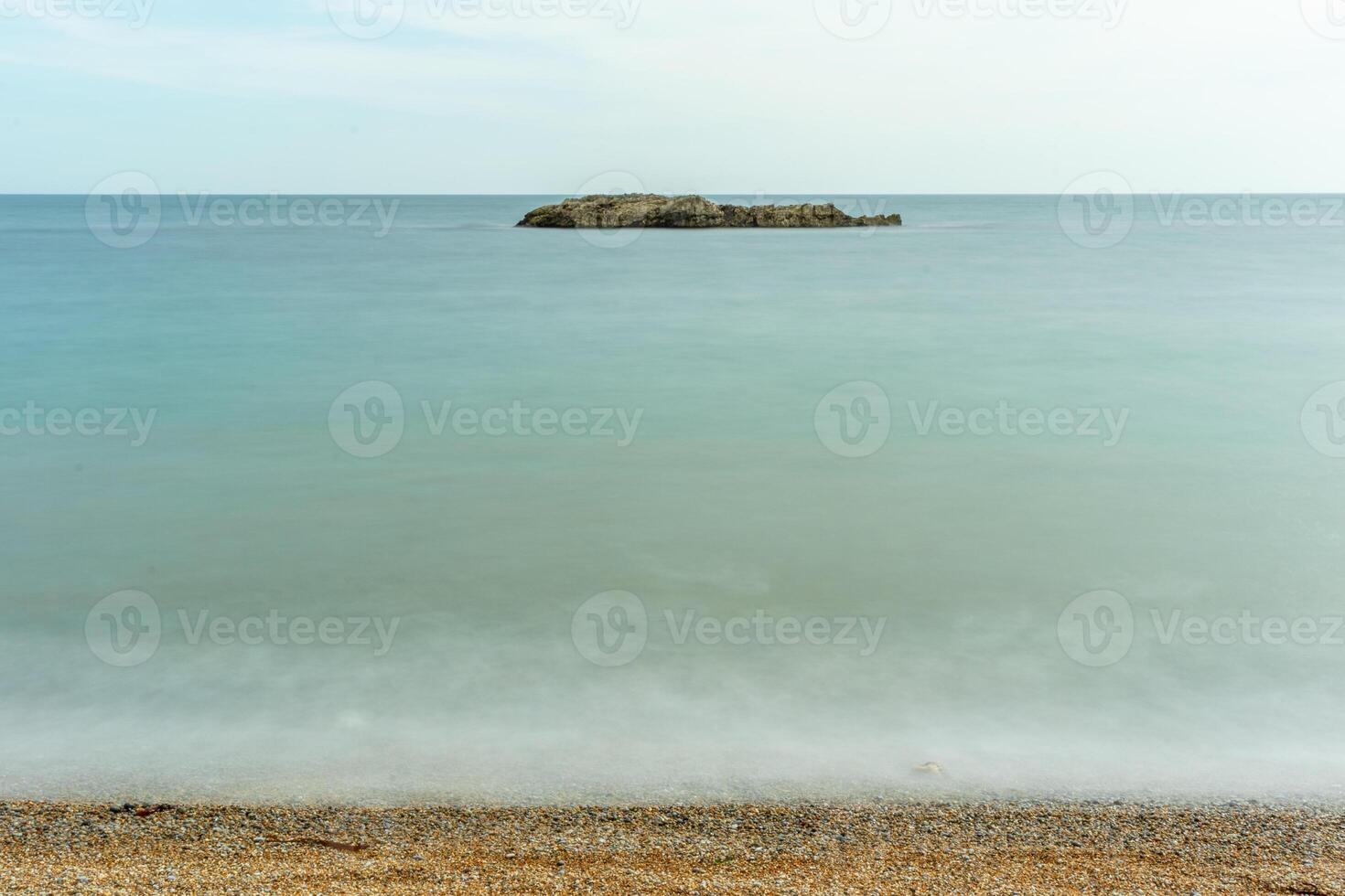 heiter Seelandschaft mit ein klein Insel auf das Horizont, Ruhe Blau Wasser, und ein Kieselstein Strand im das Vordergrund beim durdle Tür, England. foto