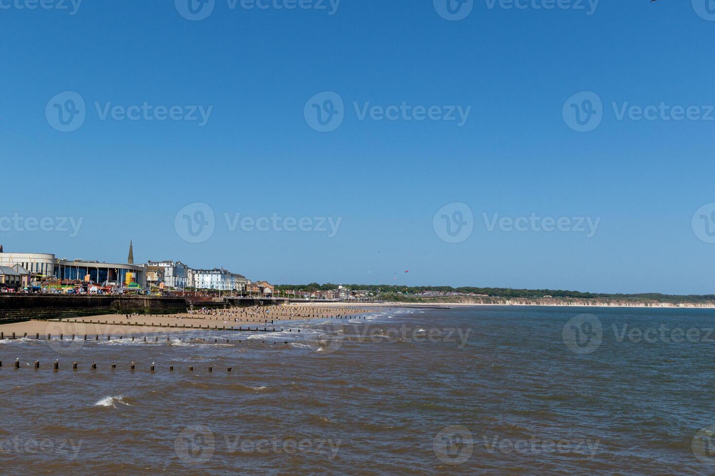 sonnig Strandlandschaft mit klar Blau Himmel, Ruhe Meer, und ein Küsten Stadt, Dorf im das Hintergrund im Bridlington, England. foto