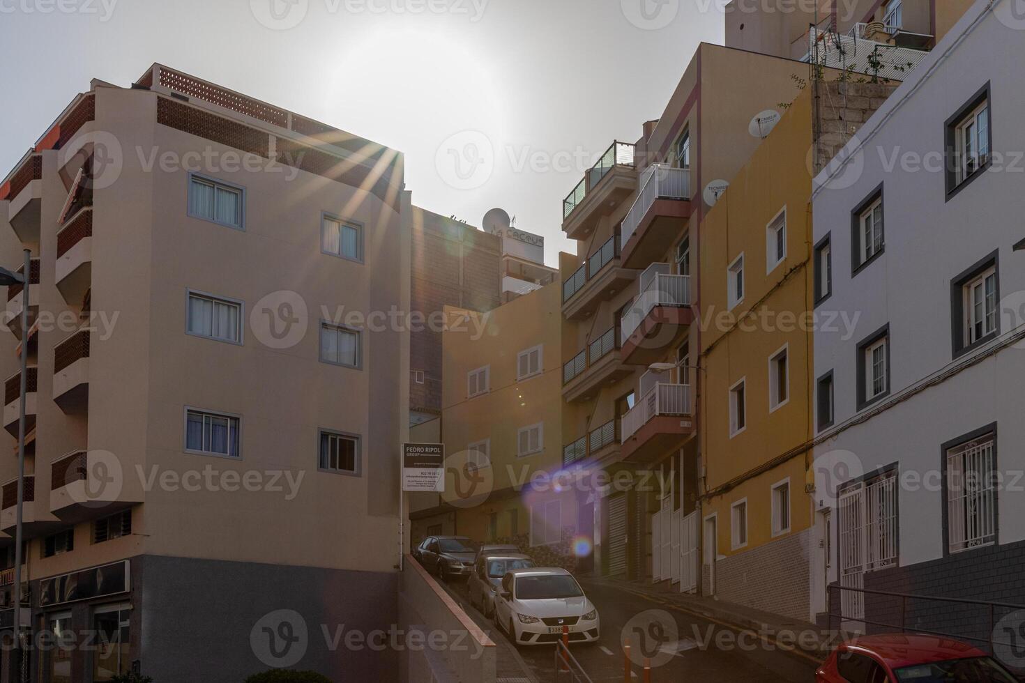 Sonne Fackel Über städtisch Straße mit modern Wohnung Gebäude und geparkt Autos, abbilden Stadt Leben im los Cristianos, Teneriffa. foto