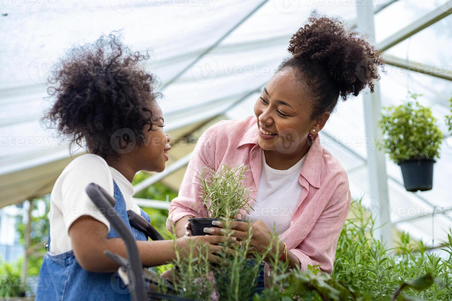 afrikanische mutter und tochter wählen gemüse- und kräuterpflanzen aus der örtlichen gärtnerei mit einkaufswagen voller sommerpflanzen für wochenendgärtnern und im freien foto