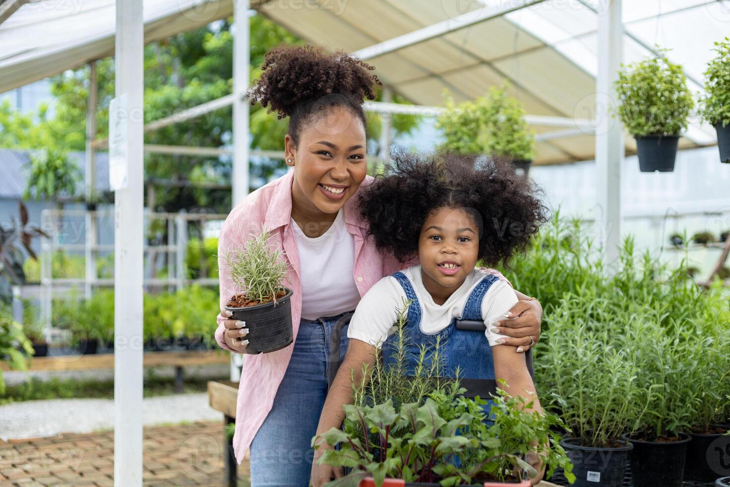 afrikanische mutter und tochter wählen gemüse- und kräuterpflanzen aus der örtlichen gärtnerei mit einkaufswagen voller sommerpflanzen für wochenendgärtnern und im freien foto