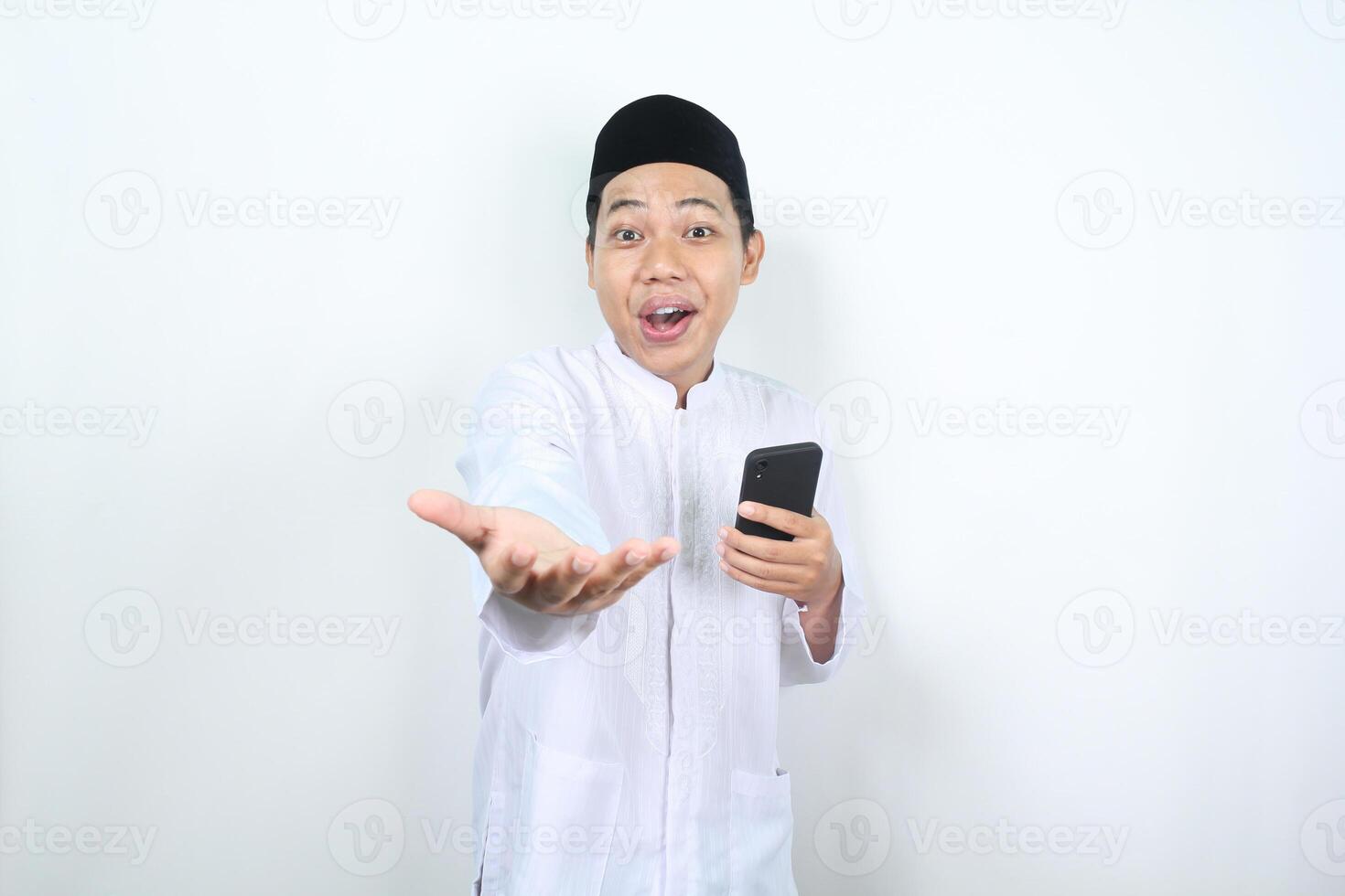 überrascht Muslim asiatisch Mann halten Handy, Mobiltelefon Telefon und erziehen Hand zu präsentieren nach vorne beim Kamera isoliert foto