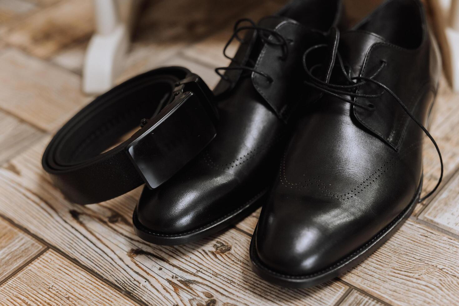 auf das Fußboden sind Herren dunkel Leder Schuhe und ein schwarz Gürtel, ein des Mannes passen auf ein Mannequin, ein Hochzeit Strauß von Blumen, Hochzeit Ringe, Herren Parfüm. Foto, oben Sicht. foto