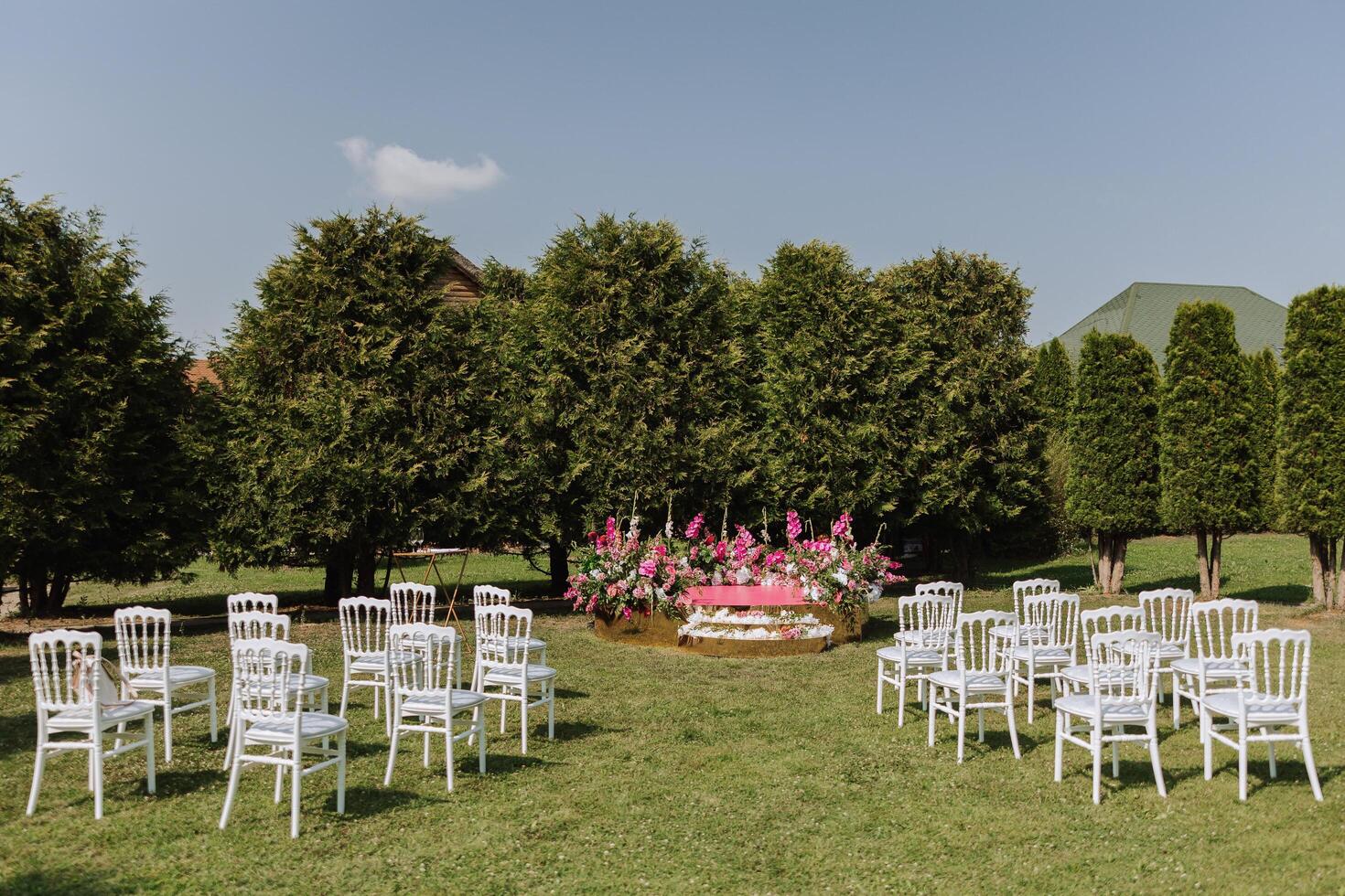 das Rosa Bühne ist dekoriert mit Blumen auf das Hintergrund von das Wald. viele Weiß Stühle auf Grün Gras. Vorbereitung zum das Hochzeit Zeremonie foto