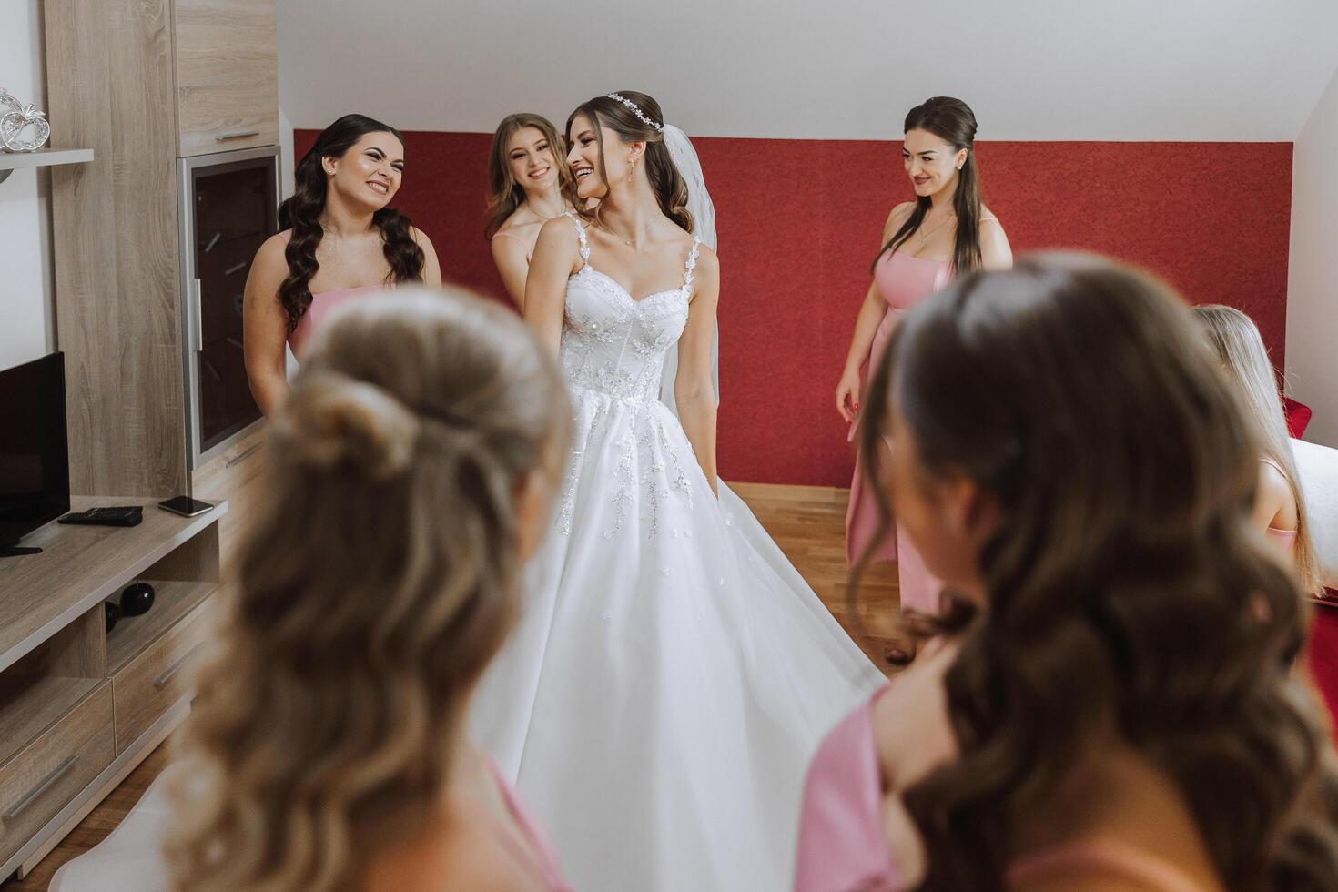 Hochzeit Morgen. Brautjungfern Hilfe stellen auf das Weiß Hochzeit Kleid. ein jung Frau ist vorbereiten zu Treffen ihr Bräutigam und haben Spaß mit ihr freunde foto