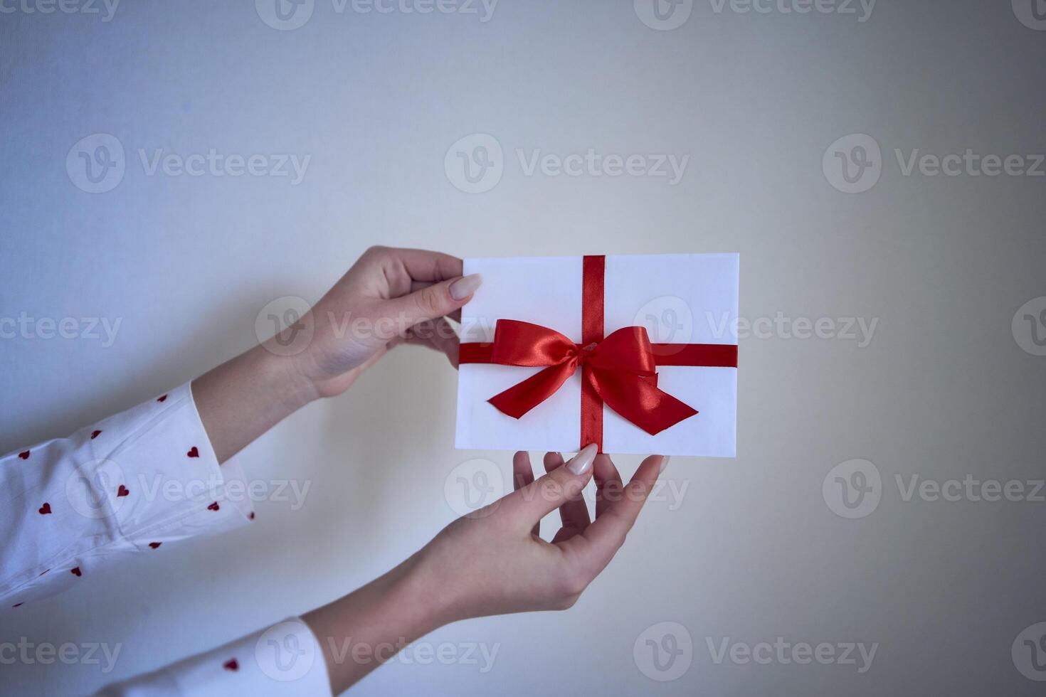 Geschenk Zertifikat im rot und Weiß Farben im weiblich Hände auf ein Weiß Mauer Hintergrund foto