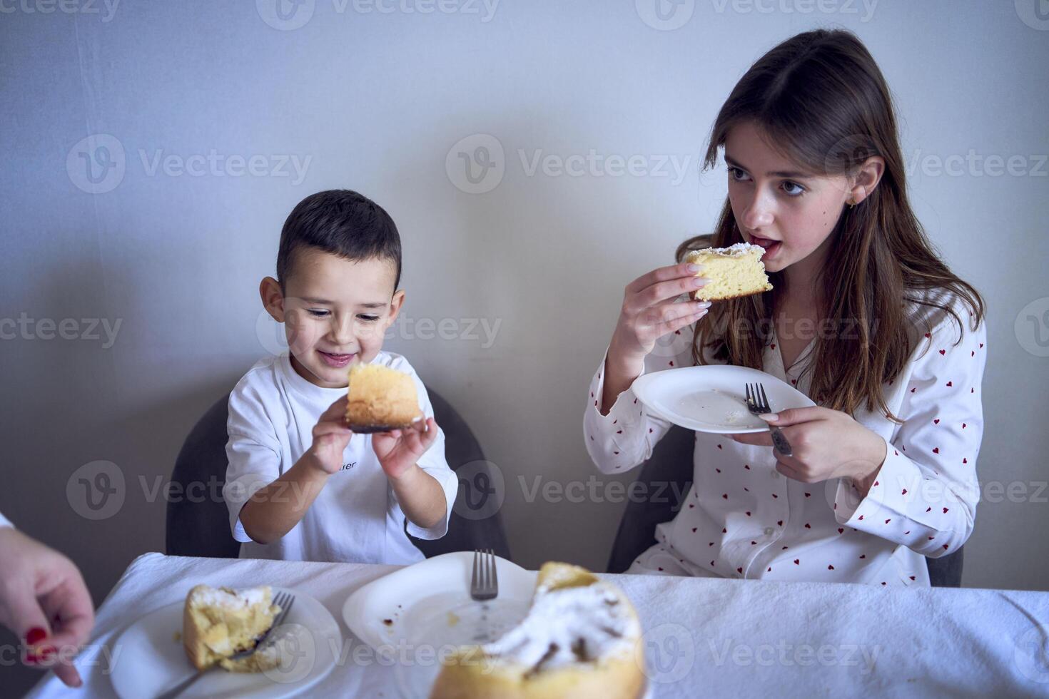 Familie von drei, Mutter, Teenager Tochter und wenig Sohn, Essen Kuchen im Pyjama beim ein Tabelle mit Tulpen foto