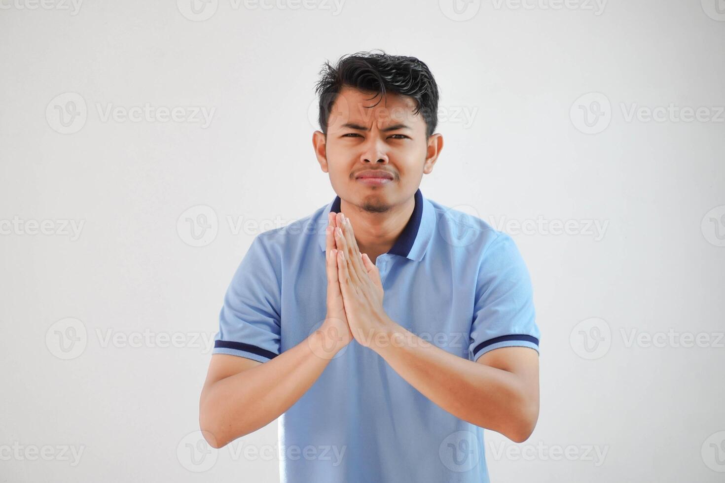 jung asiatisch Mann tragen beiläufig Blau t Hemd Über Weiß Hintergrund betteln mit Hände zusammen mit hoffen Ausdruck auf Gesicht sehr emotional und besorgt. betteln. traurig Gesicht foto