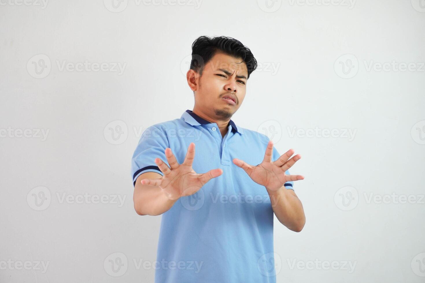 attraktiv asiatisch Mann mit Hand Geste Pose Ablehnung oder Verbot während zeigen zu Kopieren Raum durch seine Vorderseite tragen Blau t Hemd isoliert auf Weiß Hintergrund foto