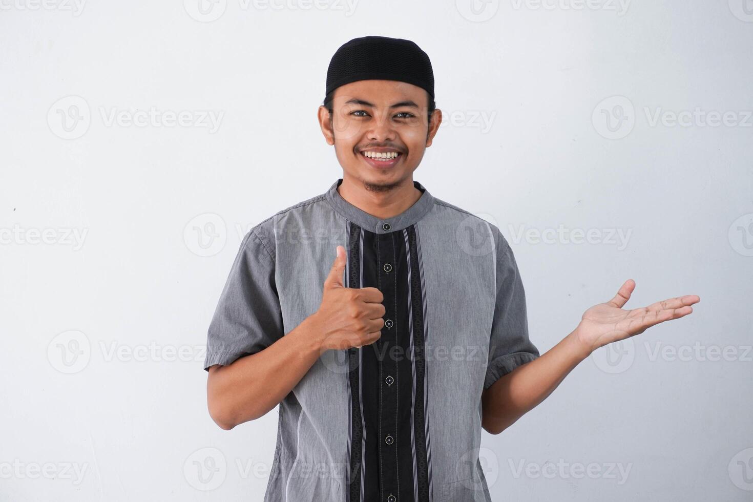 lächelnd oder glücklich jung asiatisch Muslim Mann zeigen Palme Hand und tun in Ordnung Geste mit Daumen oben tragen koko Kleider isoliert auf Weiß Hintergrund foto