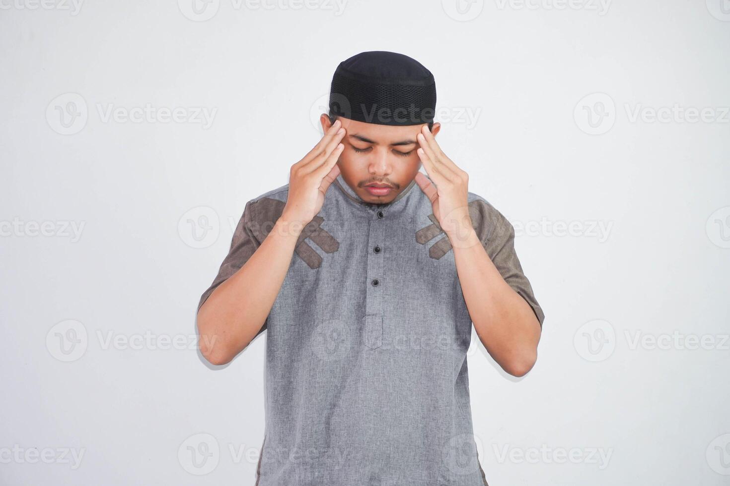 jung asiatisch Muslim Mann halten seine Kopf Leiden Kopfschmerzen tragen grau Muslim Kleider isoliert auf Weiß Hintergrund foto