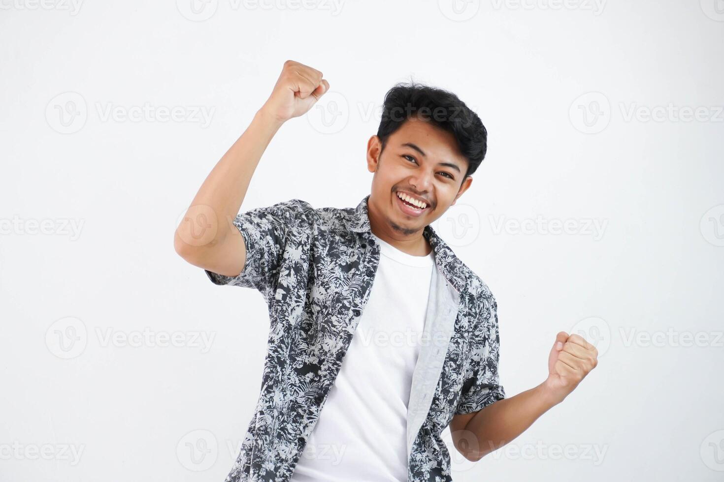 zuversichtlich heiter gut aussehend asiatisch Mann Heben Hände oben tragen schwarz Hemd fühlt sich Glück Show Faust oben Erfolg isoliert auf Weiß Hintergrund foto