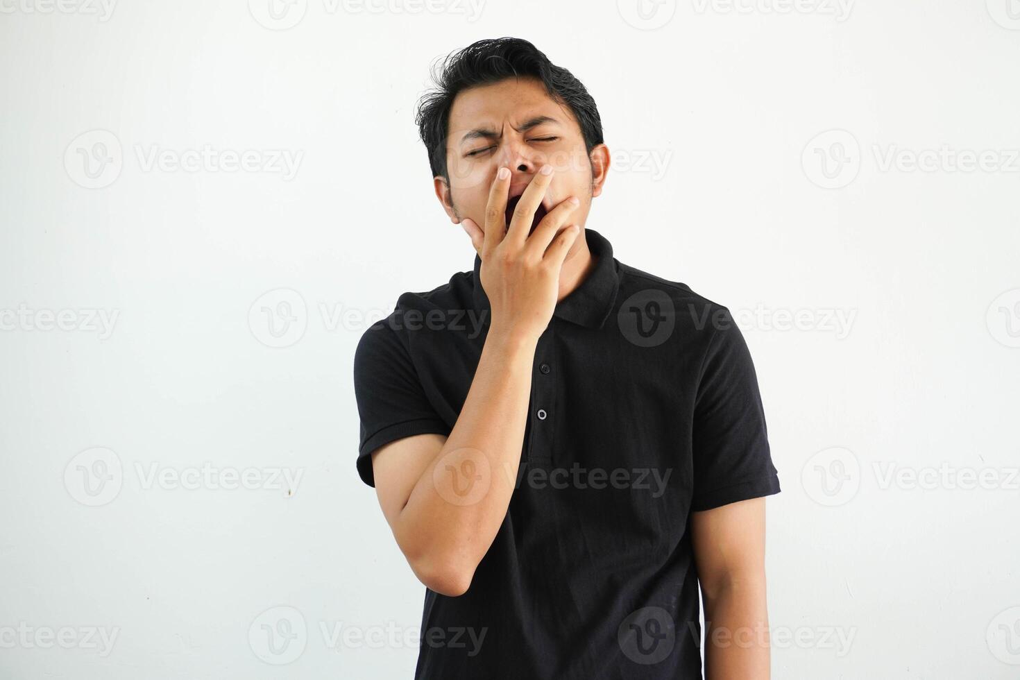 schläfrig jung asiatisch Mann Gähnen durch Abdeckung Mund mit Hand tragen schwarz Polo t Hemd isoliert auf Weiß Hintergrund foto