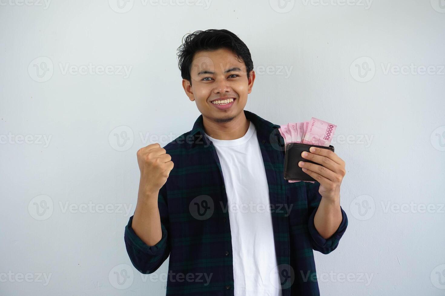 jung asiatisch Mann zeigen aufgeregt Gesicht Ausdruck während halten seine Brieftasche voll von Geld mit geballt Fäuste isoliert auf Weiß Hintergrund foto