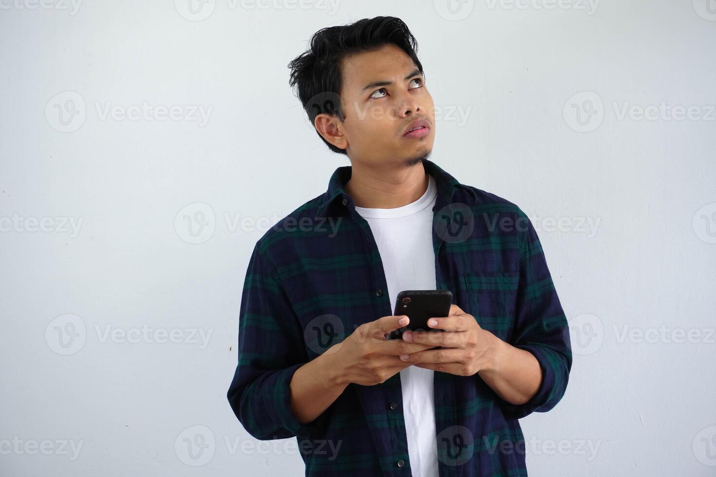jung asiatisch Mann denken etwas während Tippen auf seine Handy, Mobiltelefon Telefon isoliert auf Weiß Hintergrund. foto