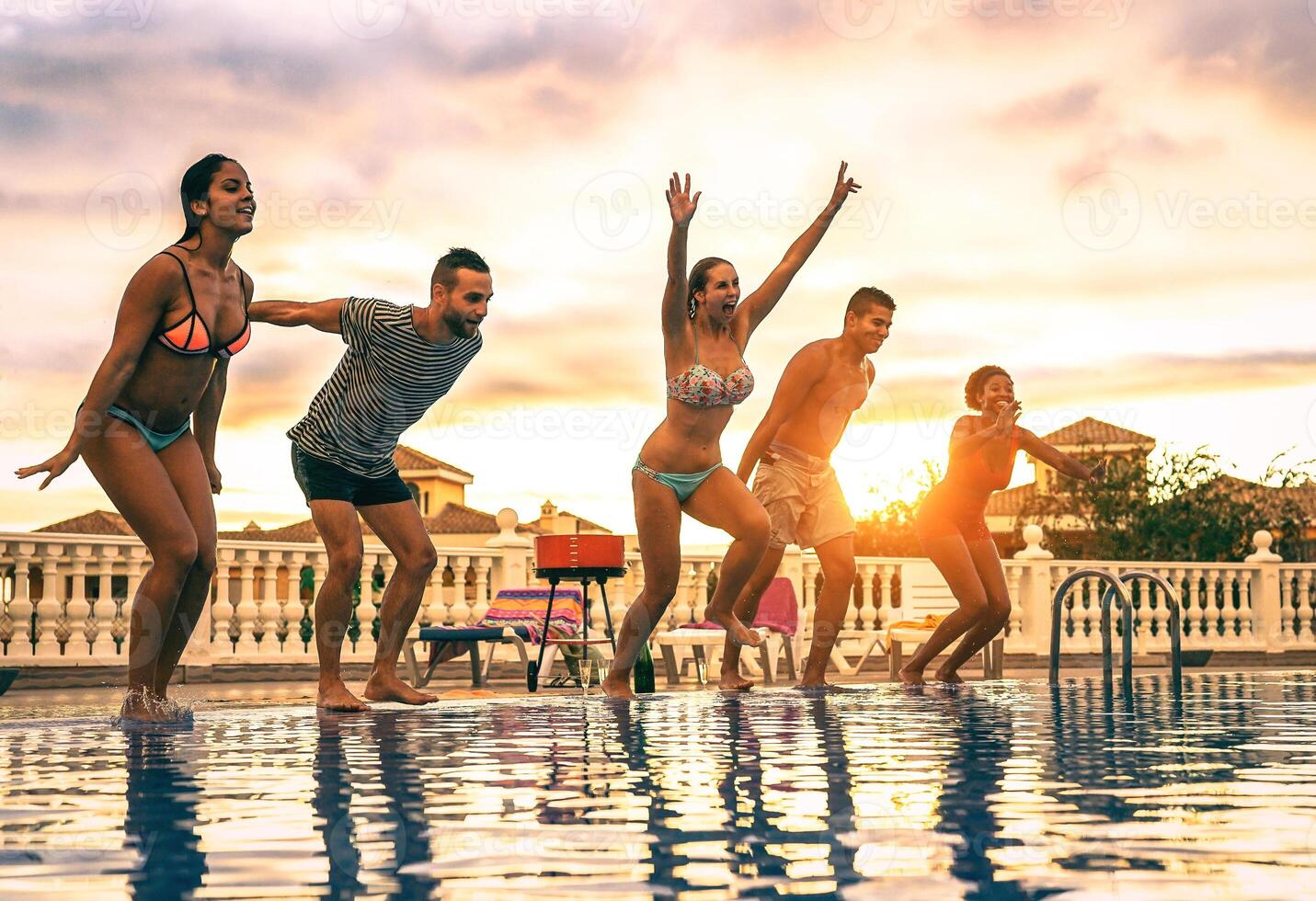 Gruppe von glücklich freunde Springen im das Schwimmbad beim Sonnenuntergang - - jung Menschen haben Spaß Herstellung Party im exklusiv Resort tropisch im Ferien - - Konzept von Freundschaft, Ferien und Jugend Lebensstil foto