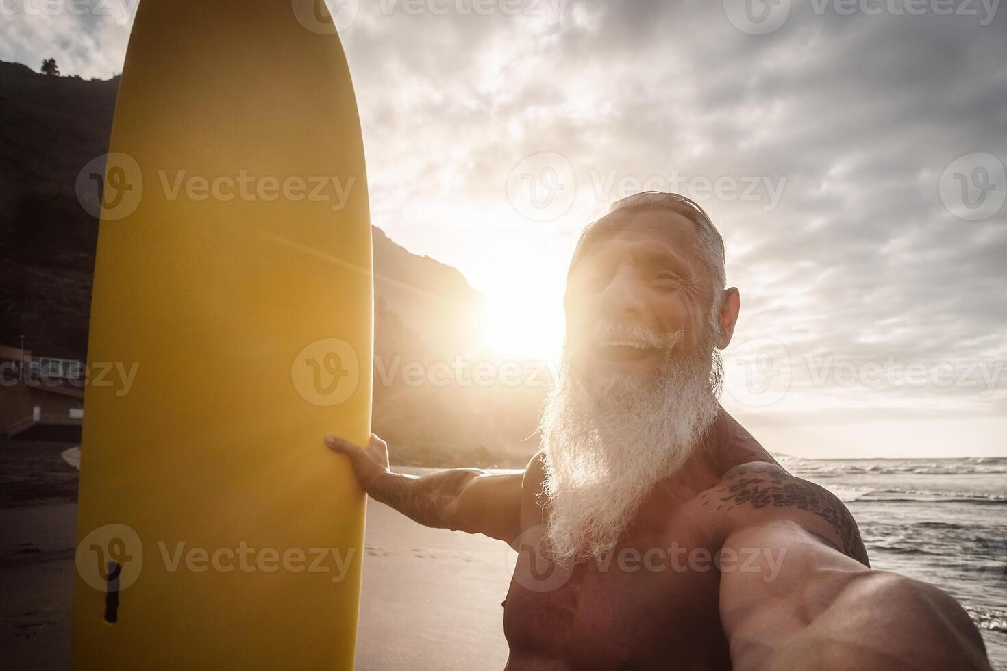 glücklich passen Senior haben Spaß Surfen beim Sonnenuntergang Zeit - - sportlich bärtig Mann nehmen Selfie während Ausbildung mit Surfbrett auf das Strand - - Alten gesund Menschen Lebensstil und extrem Sport Konzept foto