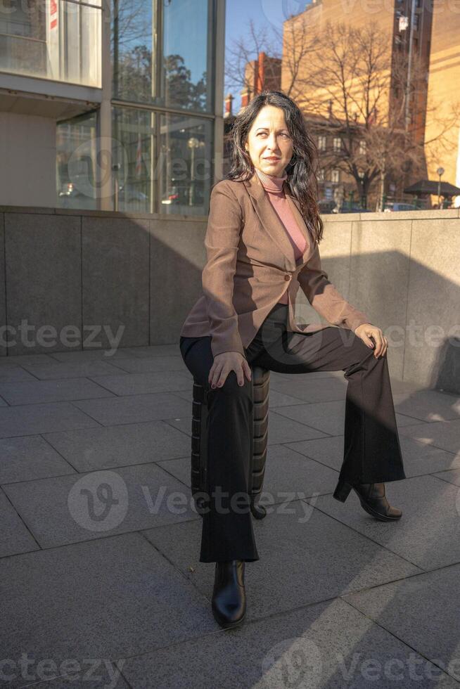 jung Frau gekleidet im passen warten zum ein Taxi Sitzung auf ein schwarz Koffer foto