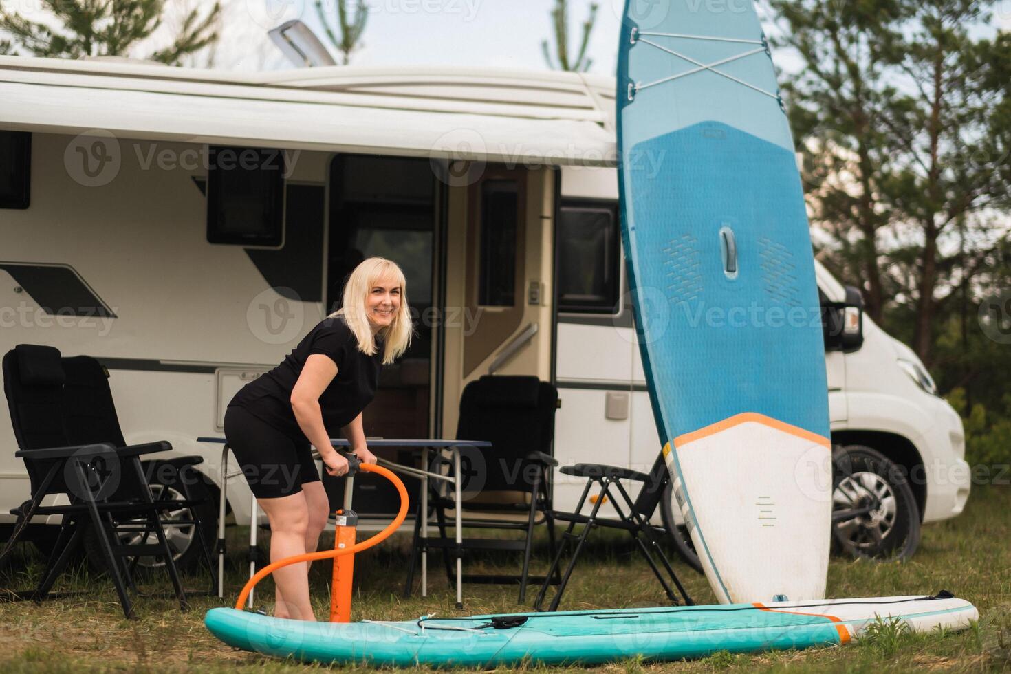 ein Frau bläst auf ein Sup-Board zum Schwimmen in der Nähe von ihr Wohnmobil foto